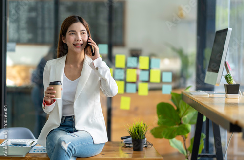 Charming Asian woman with a smile standing holding papers and mobile phone at the office.