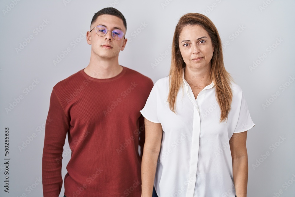 Mother and son standing together over isolated background relaxed with serious expression on face. simple and natural looking at the camera. Mother and son standing together over isolated background relaxed with serious expression on face. simple and natural looking at the camera.