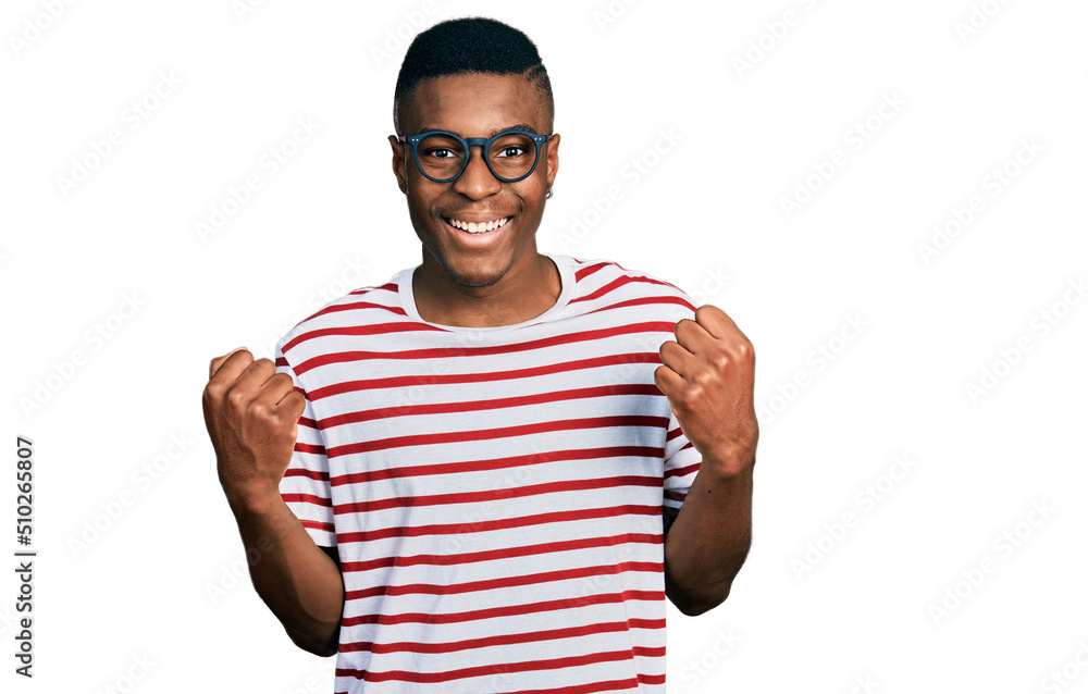 Naklejka premium Young african american man wearing casual t shirt and glasses celebrating surprised and amazed for success with arms raised and open eyes. winner concept.
