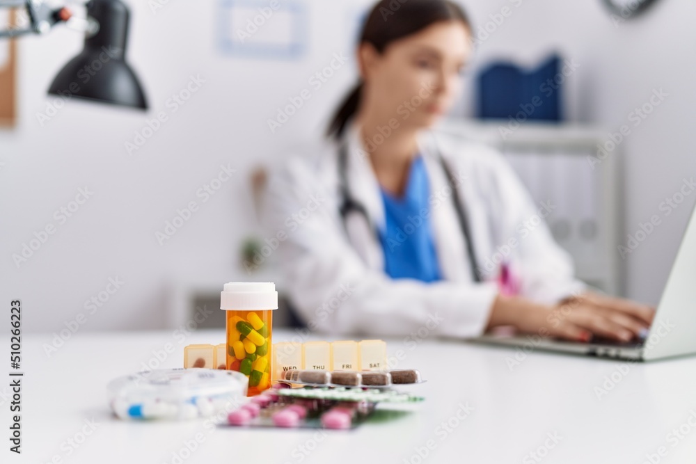 Fototapeta premium Young hispanic woman wearing doctor uniform prescribing pills at hospital