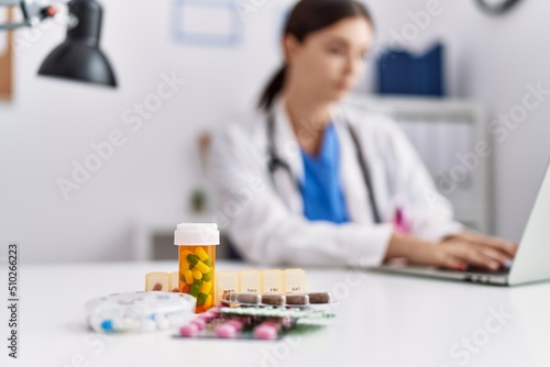 Young hispanic woman wearing doctor uniform prescribing pills at hospital