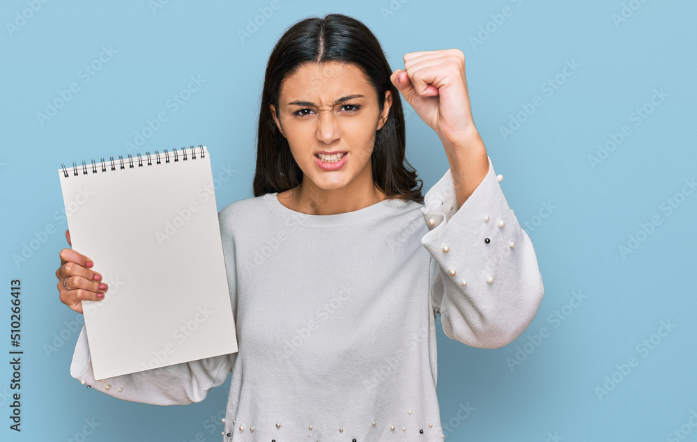 Young hispanic girl holding notebook annoyed and frustrated shouting with anger, yelling crazy with anger and hand raised Young hispanic girl holding notebook annoyed and frustrated shouting with anger, yelling crazy with anger and hand raised