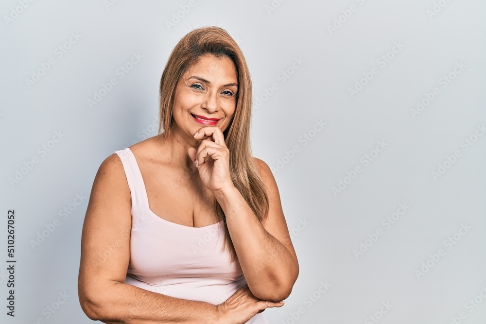 Middle age hispanic woman wearing casual style with sleeveless shirt looking confident at the camera with smile with crossed arms and hand raised on chin. thinking positive. Middle age hispanic woman wearing casual style with sleeveless shirt looking confident at the camera with smile with crossed arms and hand raised on chin. thinking positive.