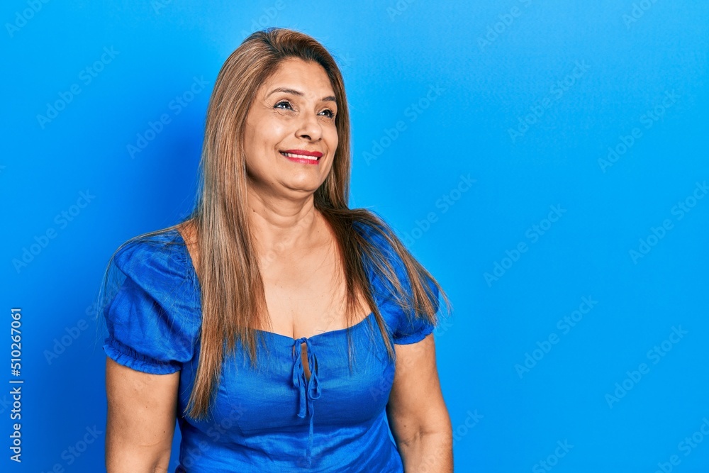 Middle age hispanic woman wearing casual clothes looking away to side with smile on face, natural expression. laughing confident. Middle age hispanic woman wearing casual clothes looking away to side with smile on face, natural expression. laughing confident.