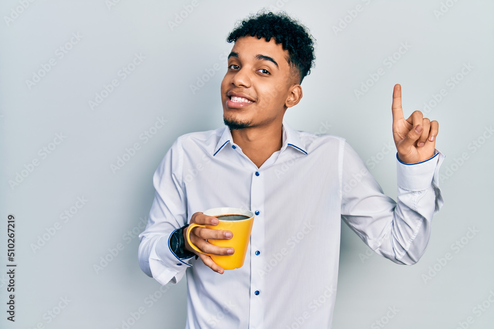 Young african american man drinking a cup of coffee smiling with an idea or question pointing finger with happy face, number one Young african american man drinking a cup of coffee smiling with an idea or question pointing finger with happy face, number one