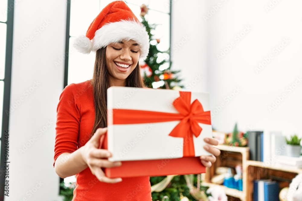 Young latin woman unboxing gift standing by christmas tree at home Young latin woman unboxing gift standing by christmas tree at home
