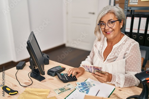 Middle age woman ecommerce business worker counting sloty banknotes at office photo