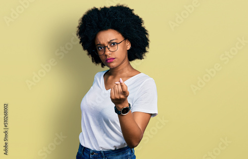 Young african american woman wearing casual white t shirt beckoning come here gesture with hand inviting welcoming happy and smiling
