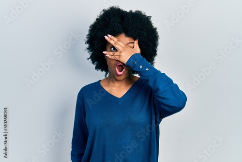 Young african american woman wearing casual clothes peeking in shock covering face and eyes with hand, looking through fingers afraid