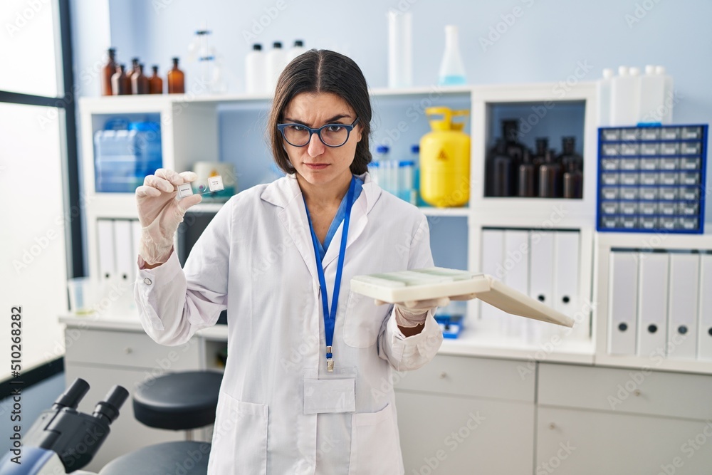 Young hispanic woman working at scientist laboratory with blood samples skeptic and nervous, frowning upset because of problem. negative person. Young hispanic woman working at scientist laboratory with blood samples skeptic and nervous, frowning upset because of problem. negative person.