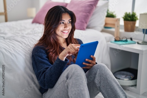 Young hispanic woman using touchpad sitting on floor at bedroom