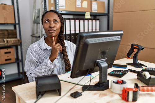 African woman working at small business ecommerce thinking concentrated about doubt with finger on chin and looking up wondering