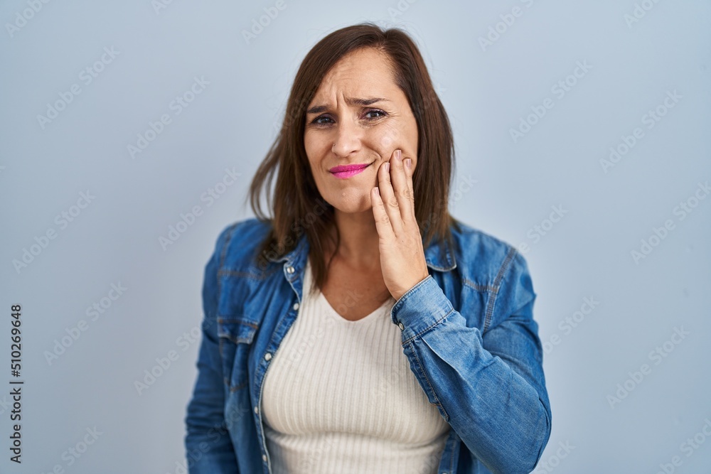 Middle age brunette woman wearing casual denim jacket over isolated background touching mouth with hand with painful expression because of toothache or dental illness on teeth. dentist Middle age brunette woman wearing casual denim jacket over isolated background touching mouth with hand with painful expression because of toothache or dental illness on teeth. dentist