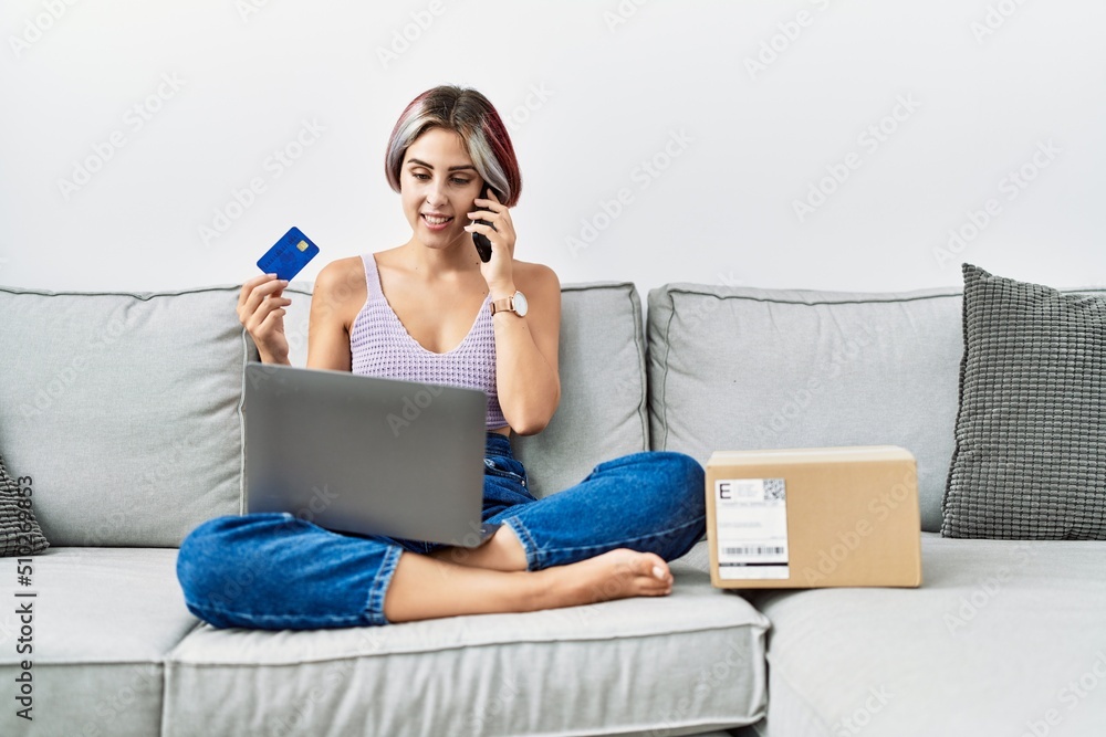 Young caucasian girl buying using laptop talking on the smartphone at home. Young caucasian girl buying using laptop talking on the smartphone at home.