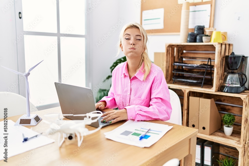 Young caucasian woman working at the office puffing cheeks with funny face. mouth inflated with air, crazy expression. Young caucasian woman working at the office puffing cheeks with funny face. mouth inflated with air, crazy expression.