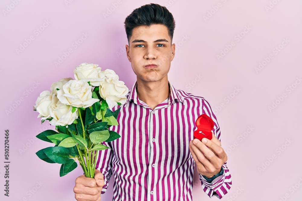 Young hispanic man holding bouquet of flowers and wedding ring puffing cheeks with funny face. mouth inflated with air, catching air. Young hispanic man holding bouquet of flowers and wedding ring puffing cheeks with funny face. mouth inflated with air, catching air.