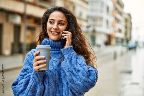 Young hispanic woman talking on the smartphone and drinking coffee at the city.