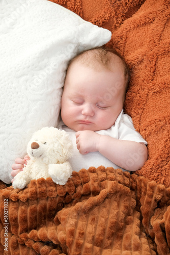 a newborn baby sleeps on a bed. A teddy bear lies nearby. mother and child. © Dmytrii