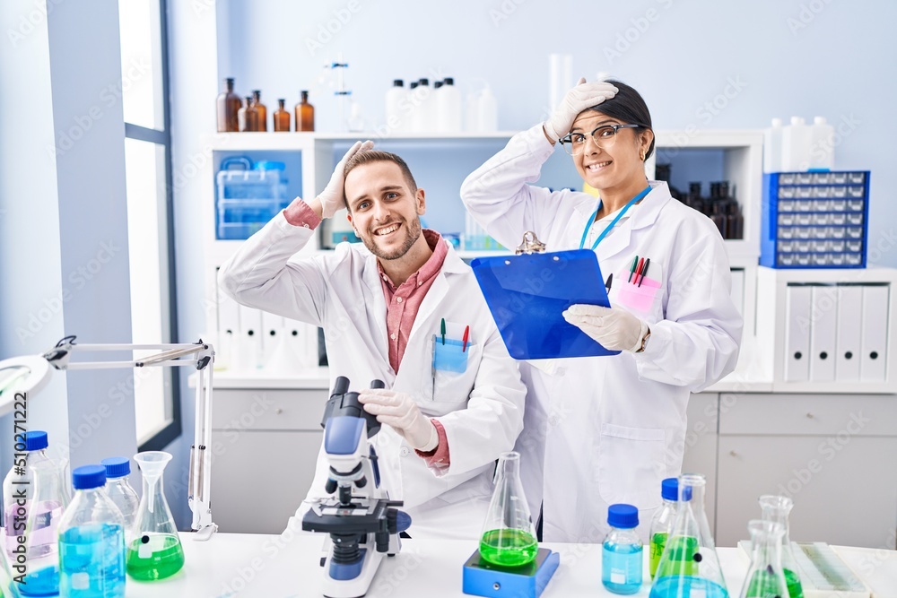 Two young people working at scientist laboratory stressed and frustrated with hand on head, surprised and angry face Two young people working at scientist laboratory stressed and frustrated with hand on head, surprised and angry face