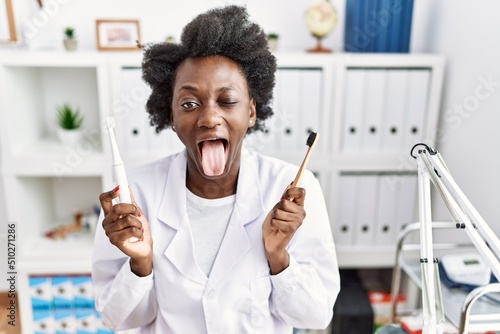 Wallpaper Mural African dentist woman holding electric toothbrush and normal toothbrush sticking tongue out happy with funny expression