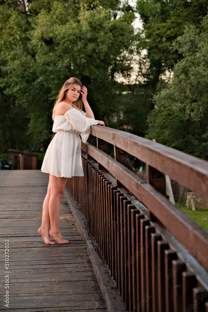 a beautiful girl in a white dress stands on a wooden bridge.