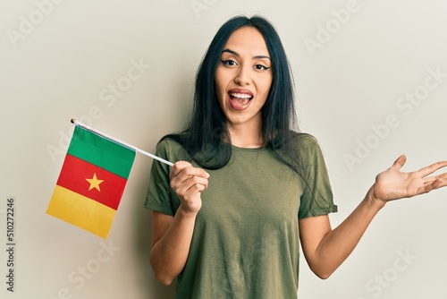 Young hispanic girl holding cameroon flag celebrating achievement with happy smile and winner expression with raised hand photo