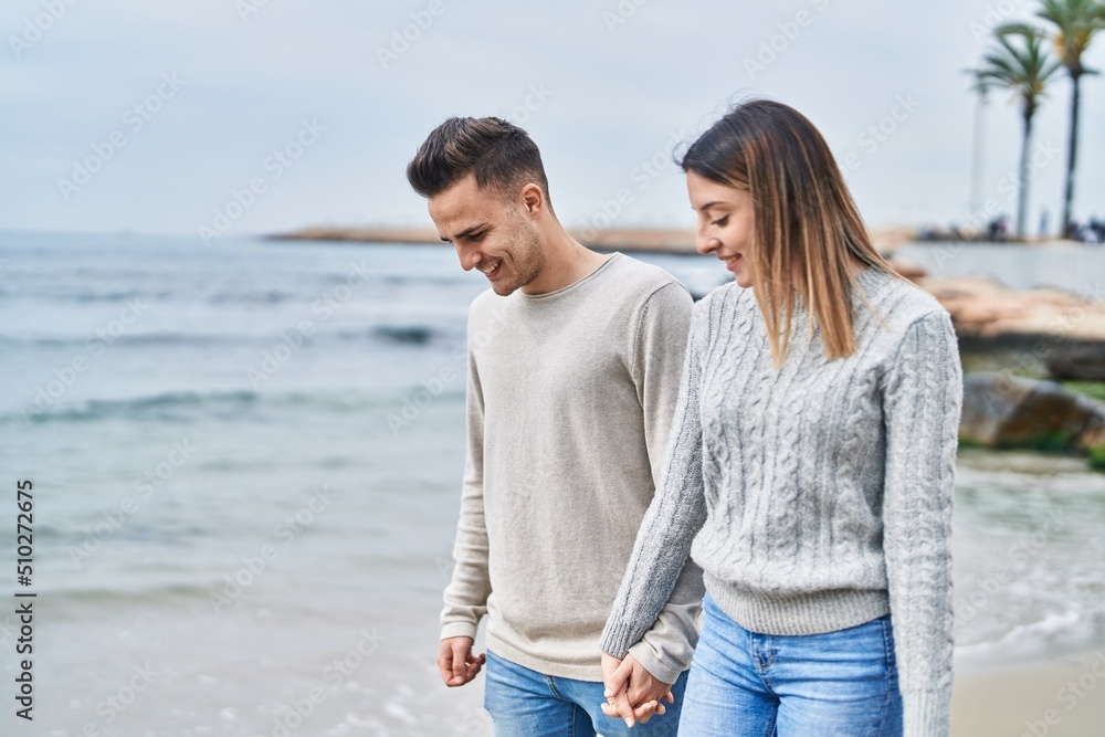 Man and woman couple smiling confident walking with hands together at seaside