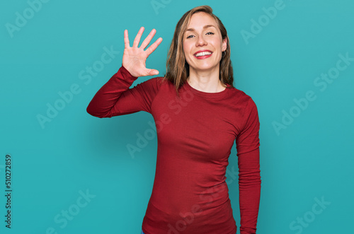 Young blonde woman wearing casual clothes showing and pointing up with fingers number five while smiling confident and happy.