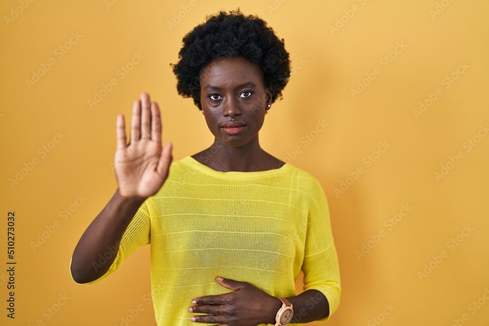 African young woman standing over yellow studio doing stop sing with palm of the hand. warning expression with negative and serious gesture on the face. African young woman standing over yellow studio doing stop sing with palm of the hand. warning expression with negative and serious gesture on the face.