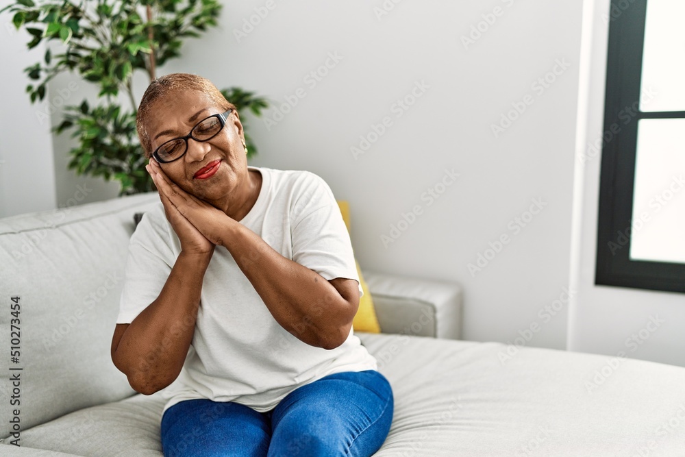 Mature hispanic woman sitting on the sofa at home sleeping tired dreaming and posing with hands together while smiling with closed eyes. Mature hispanic woman sitting on the sofa at home sleeping tired dreaming and posing with hands together while smiling with closed eyes.