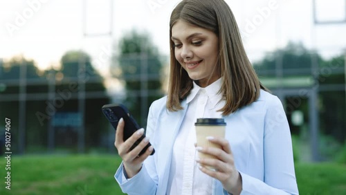 Young business woman using phone hold drink coffee in urban city buildings feel happy smile. Portrait, cellphone, street, beautiful, travel, mobile, stylish. photo