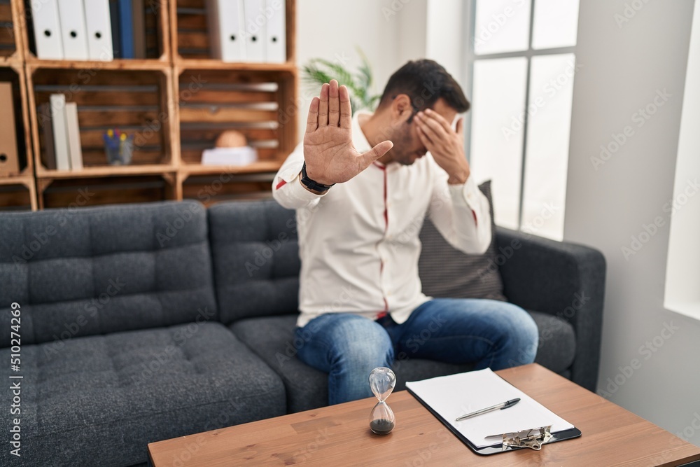 Young hispanic man with beard working at consultation office covering eyes with hands and doing stop gesture with sad and fear expression. embarrassed and negative concept. Young hispanic man with beard working at consultation office covering eyes with hands and doing stop gesture with sad and fear expression. embarrassed and negative concept.
