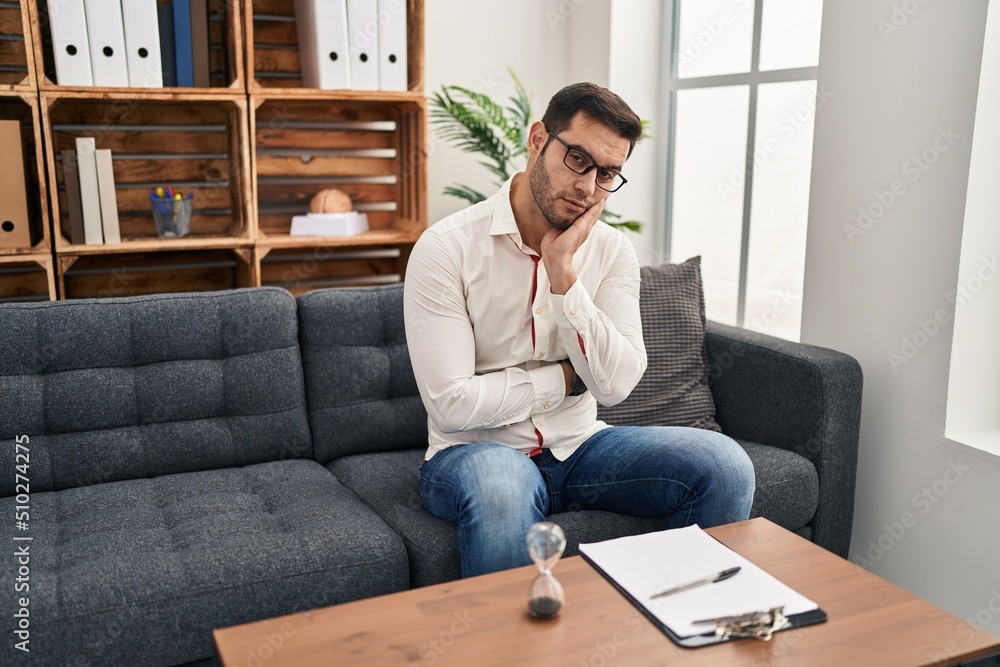 Young hispanic man with beard working at consultation office thinking looking tired and bored with depression problems with crossed arms. Young hispanic man with beard working at consultation office thinking looking tired and bored with depression problems with crossed arms.