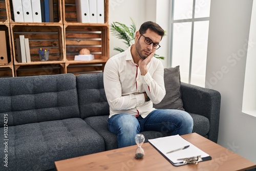 Young hispanic man with beard working at consultation office thinking looking tired and bored with depression problems with crossed arms.