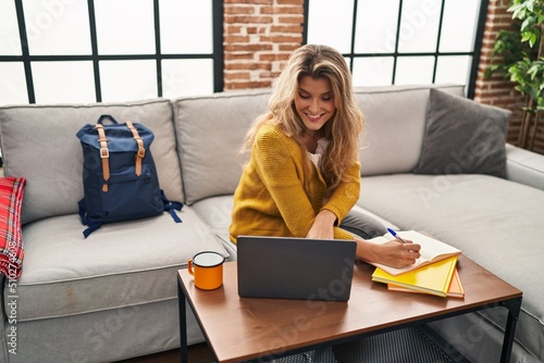 Young blonde woman smiling confident studying using laptop at home photo