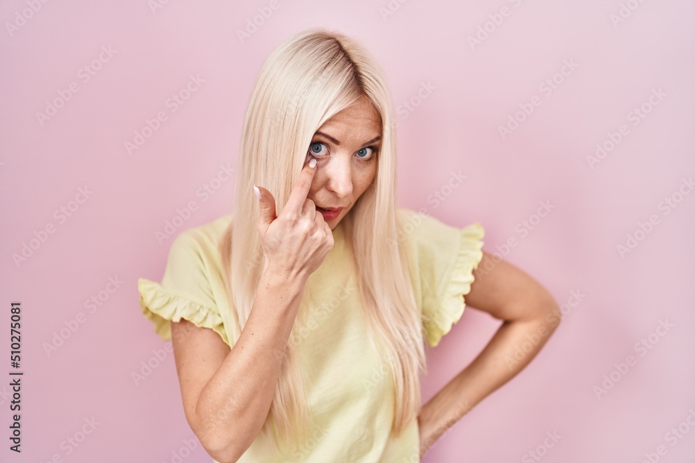 Caucasian woman standing over pink background pointing to the eye watching you gesture, suspicious expression Caucasian woman standing over pink background pointing to the eye watching you gesture, suspicious expression