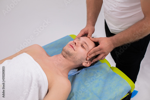 At medical clinic professional masseur man very handsome doing a head relaxed massage therapy for his client man are laying down on the massage table