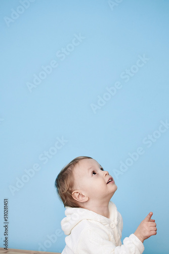 a little boy of 2 years sits in a white jacket on a blue background and thinks laughs happy sad sadness cheerful advertisement for children