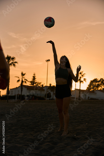 young spanish brunette woman playing volleyball at the beach while sunset