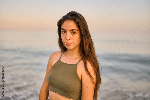 portrait of a young spanish tanned woman wearing a green top standing in front of the sea at the beach on a summer day