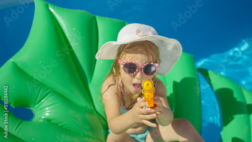 TOP DOWN Little girl sitting on a floatie with water gun pointing towards camera © helivideo