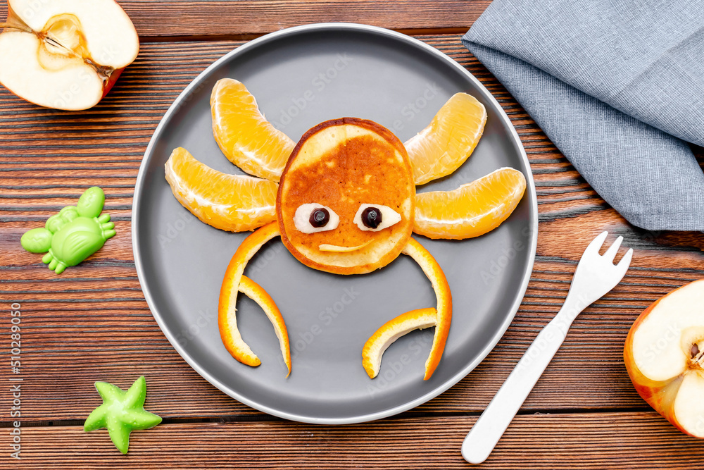 Funny crab face shape snack from pancake, orange,apples on plate. Cute kids childrens baby's sweet dessert, healthy breakfast,lunch, food art on wooden background,top view