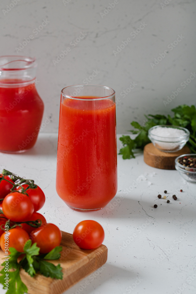 A glass of tomato juice, tomatoes in front. Behind is a jug of juice, pepper, salt and parsley. A glass of tomato juice, tomatoes in front. Behind is a jug of juice, pepper, salt and parsley.