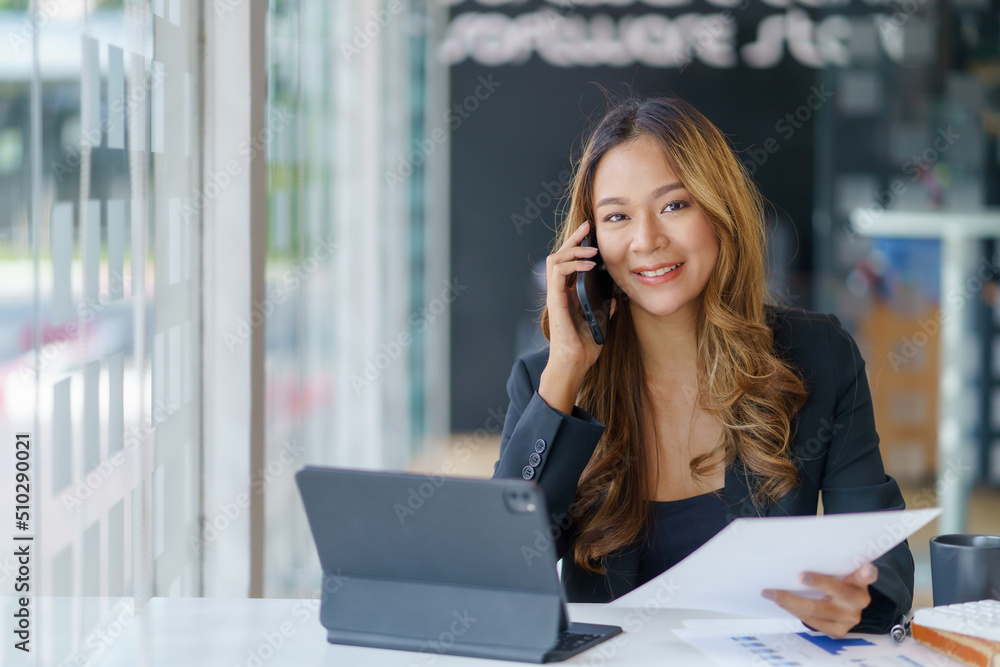 Happy secretary Asian business woman charming sitting smiling and talking on the smartphone. Looking at camera. Happy secretary Asian business woman charming sitting smiling and talking on the smartphone. Looking at camera.