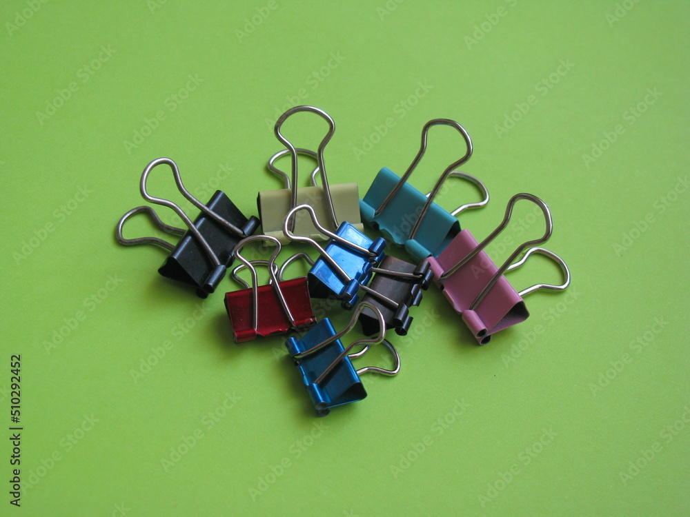 Multicolored paper clips on a light green background. Pile of colorful paper clips. Multicolored paper clips on a light green background. Pile of colorful paper clips.