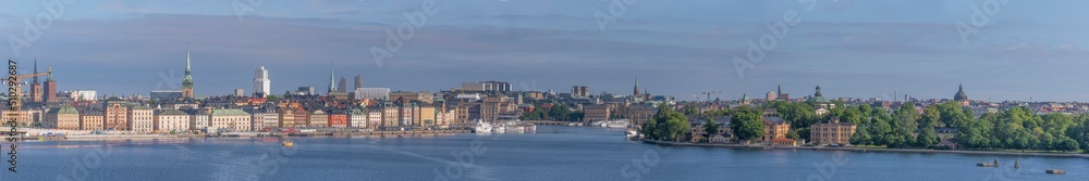 Panorama view at sunrise, the old town Gamla Stan, down town buildings, the islands Skeppsholmen and Kastellholmen at the bay Stockholms Ström with commuting boats a sunny summer day in Stockholm