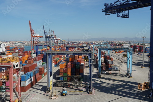 Container terminal with stowed containers from different shippers and gantry cranes in Valencia. In horizon is a city buildings and mountain under blue sky. photo