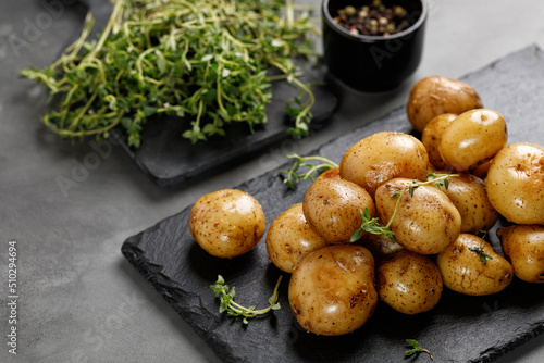 Young Fresh homemade boiled baby potatoes with thyme on slate board and dark background. Close up.