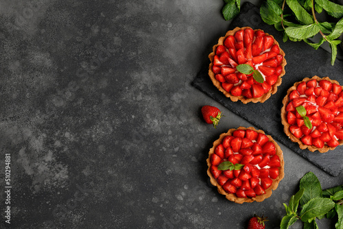 Tarts with Strawberries, cream and mint on slate board and dark background. Cake basket, dessert with strawberries. Sweet pies.