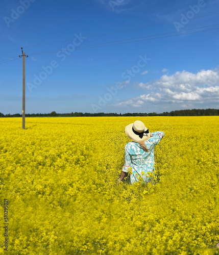 woman in wrap hat and blue dress on wild field yellow flowers and bright sky with white clouds summer nature landscape